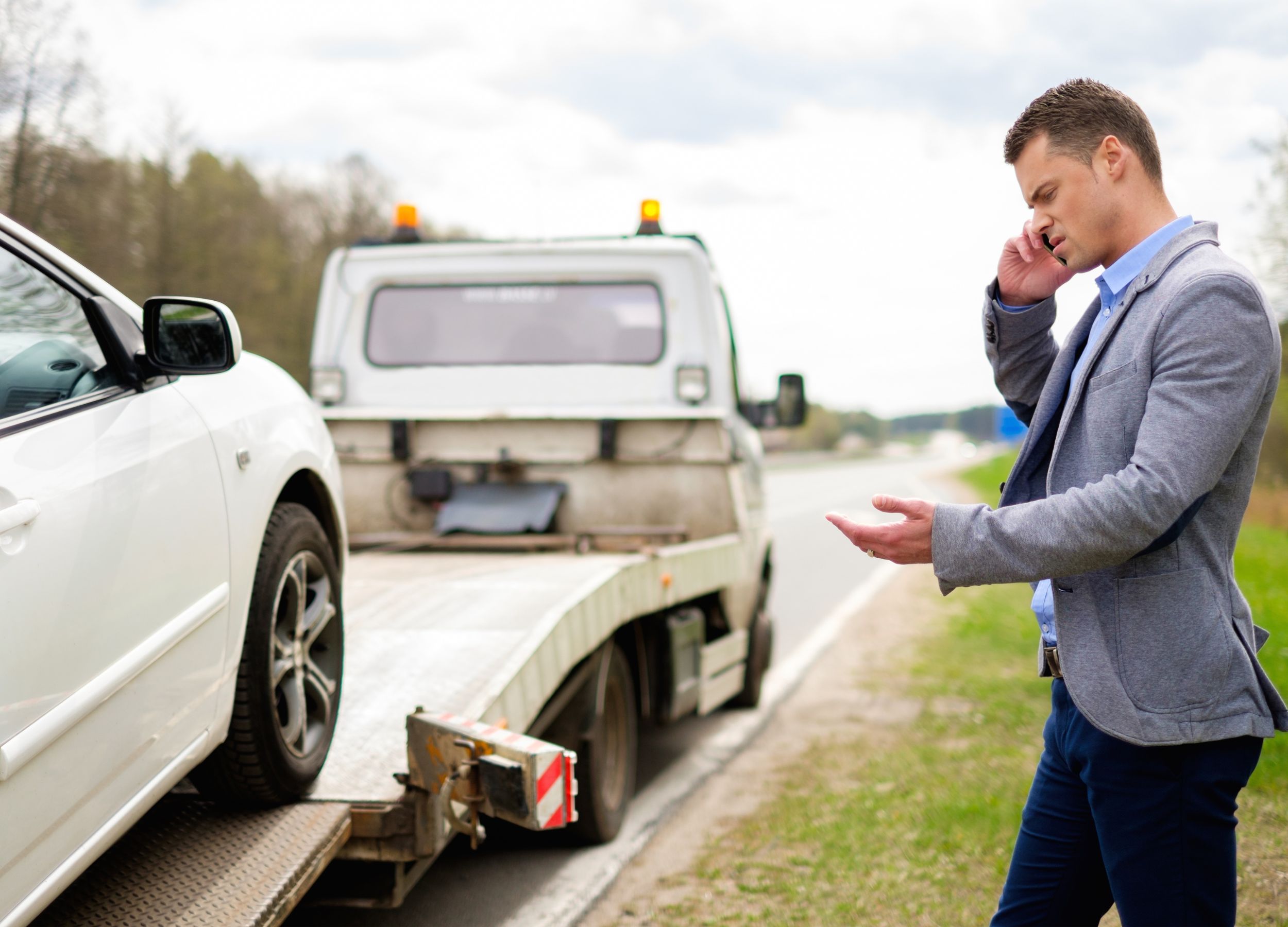 man holding phone while car is being loaded on recovery truck towing services